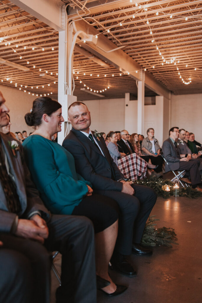 Mother and father of the bride smile as bride walks down aisle