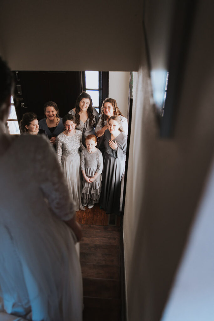 Bride walks down staircase to show dress to bridesmaids
